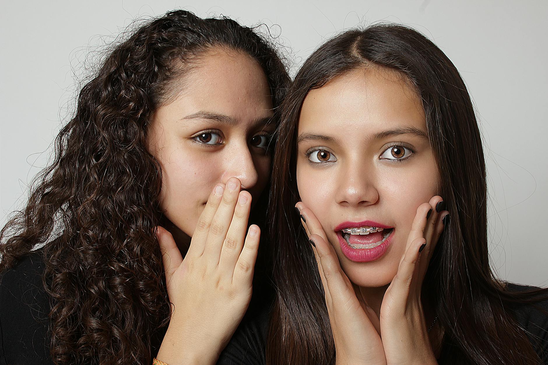 Dwie nastolatki szepczą sobie na ucho, reagując zaskoczeniem