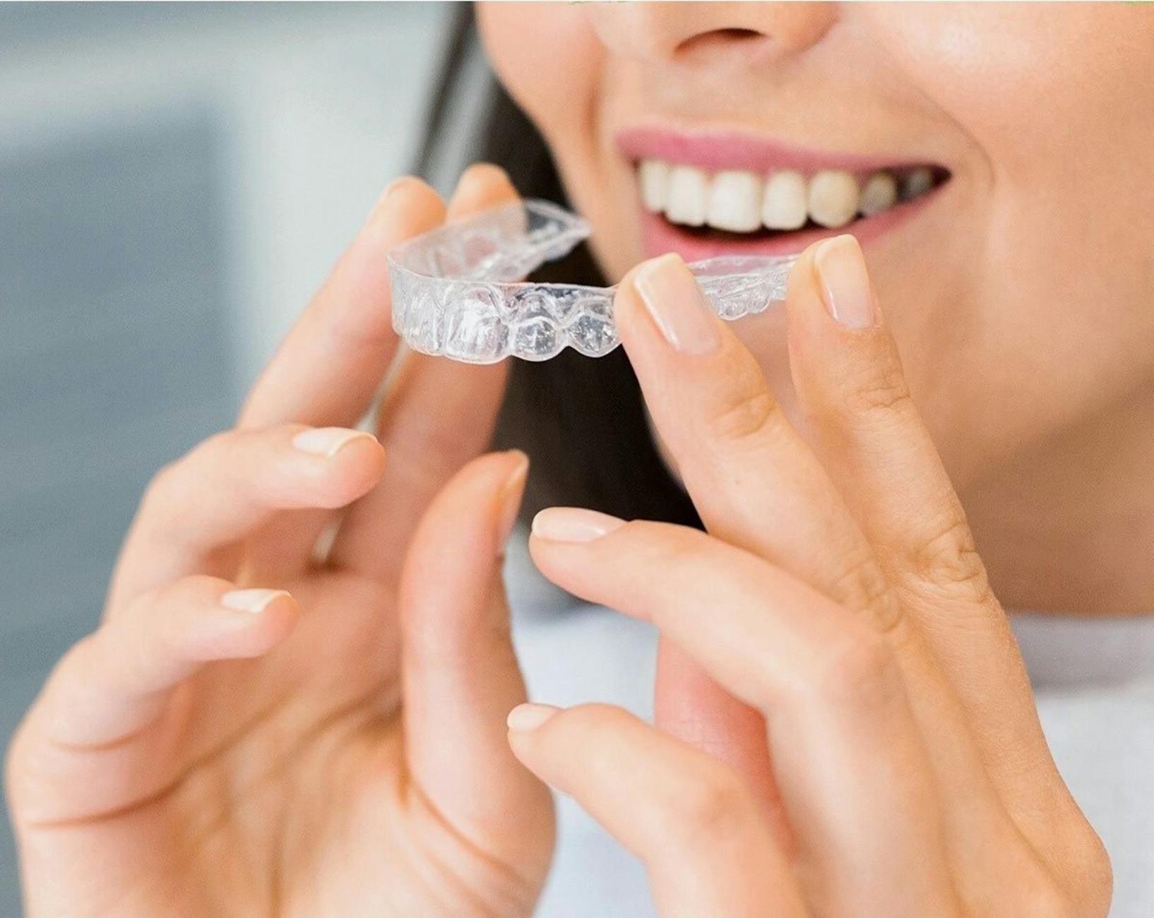Kobieta z uśmiechem trzyma przezroczystą nakładkę Invisalign