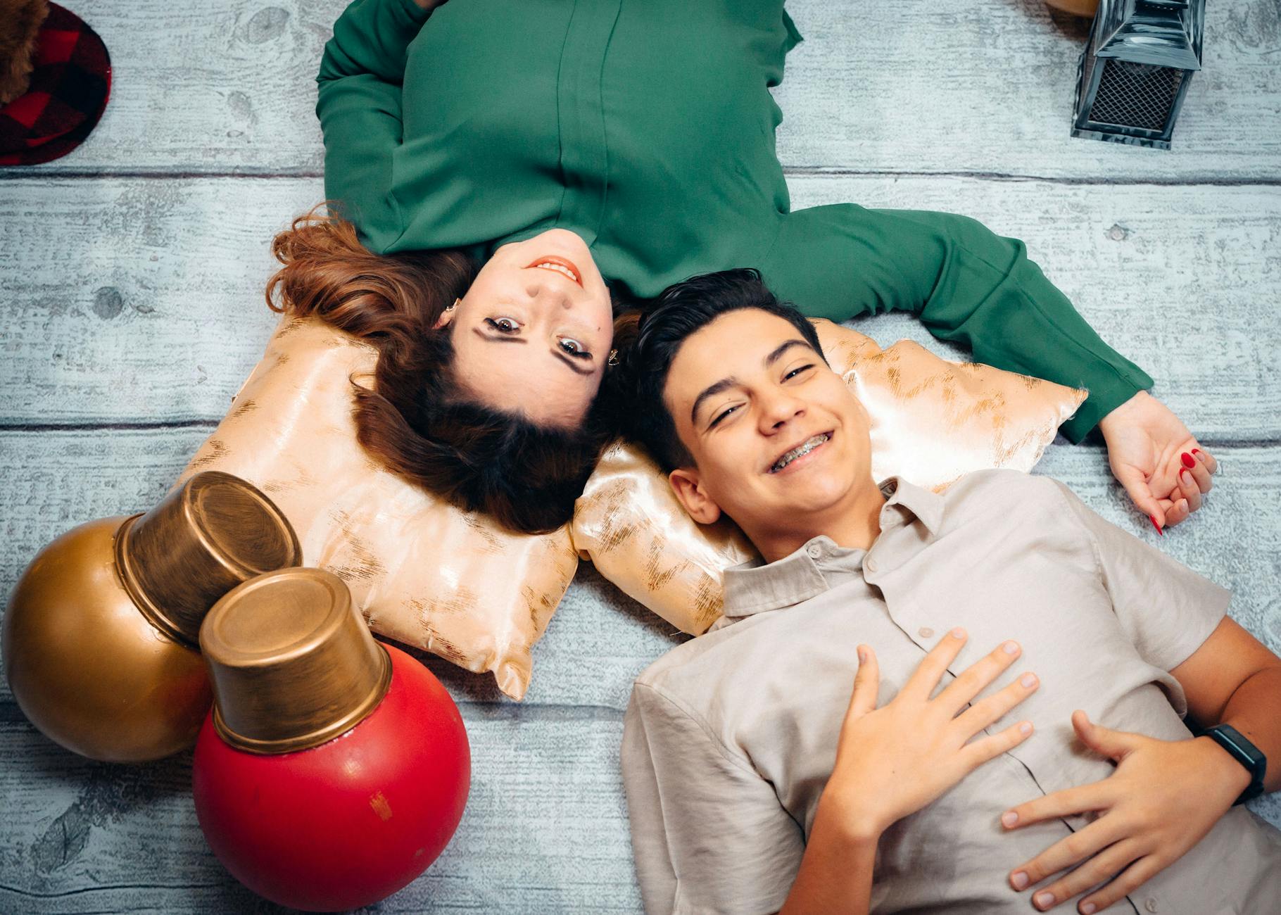 Uśmiechnięta para leży na drewnianej podłodze wśród świątecznych ozdób