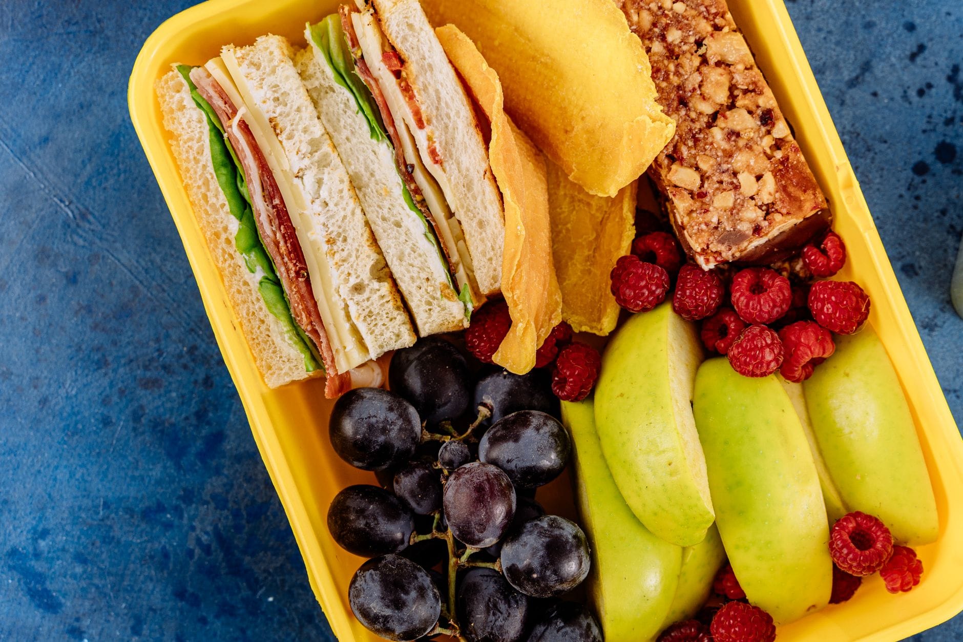 Kolorowy lunchbox z kanapką, świeżymi owocami i zdrowym batonem