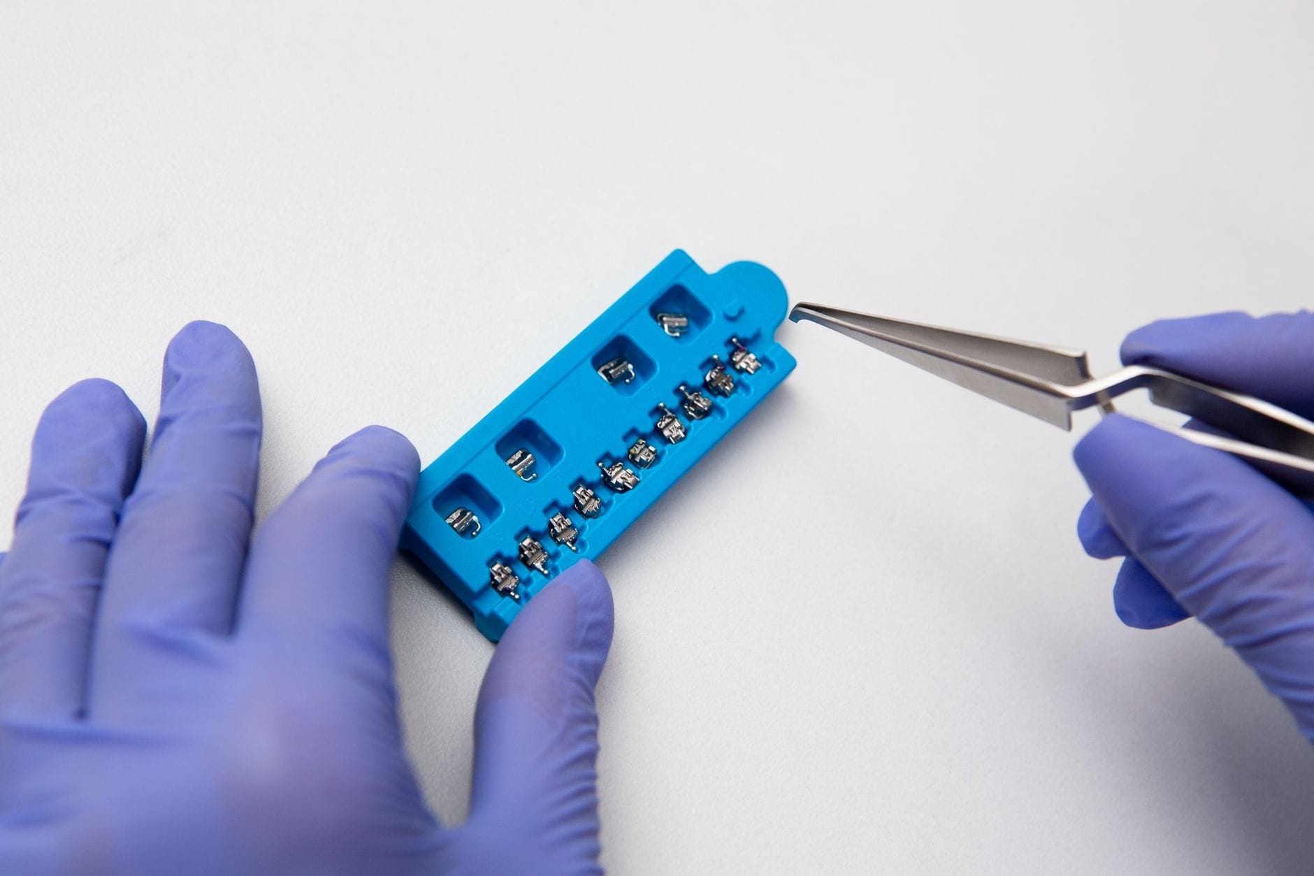Dentysta w fioletowych rękawiczkach trzyma pęsetę i metalowy aparat