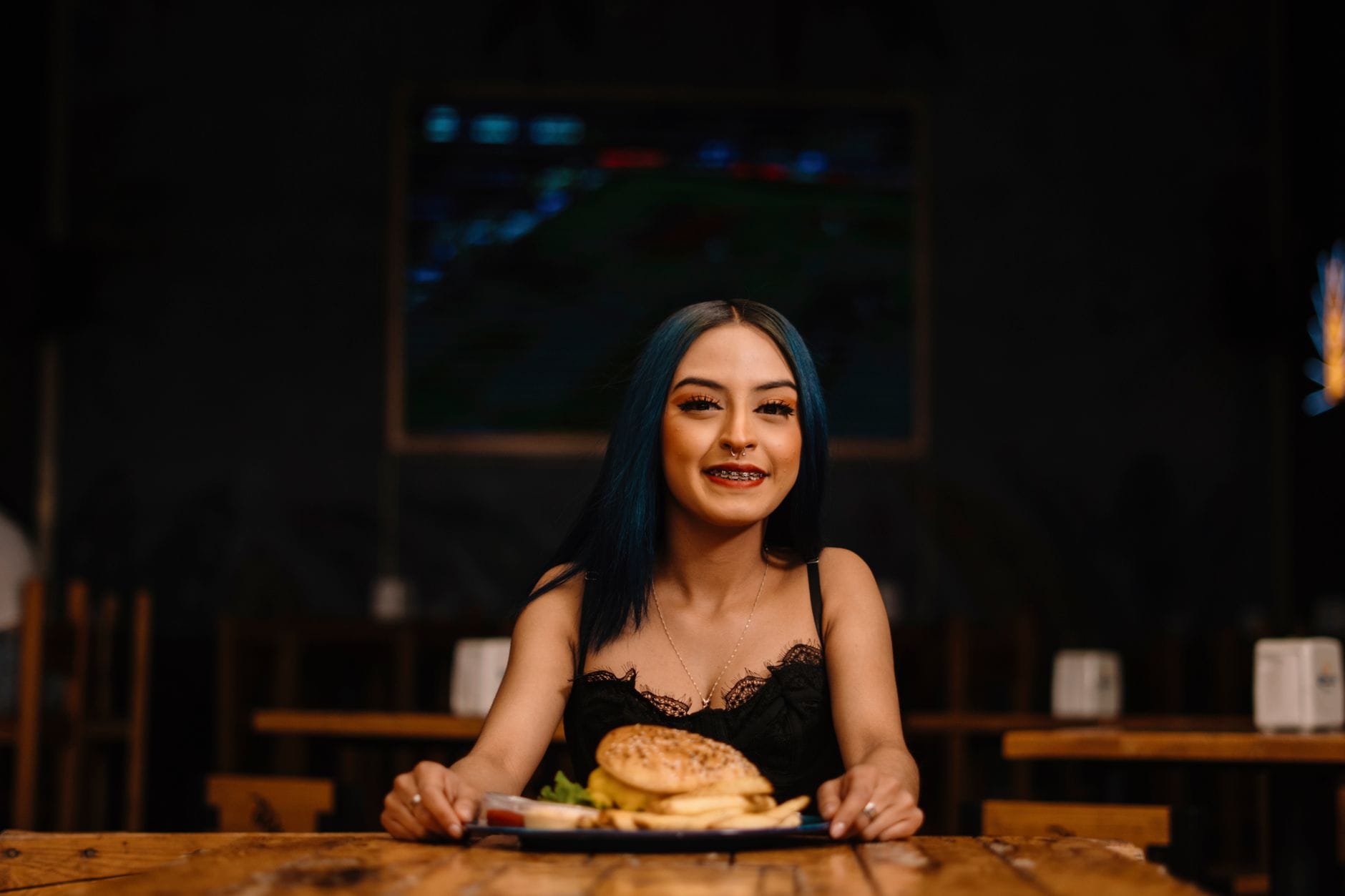 Uśmiechnięta kobieta z aparatem ortodontycznym trzyma burgera w restauracji Uśmiechnięta kobieta z aparatem ortodontycznym trzyma burgera w restauracji